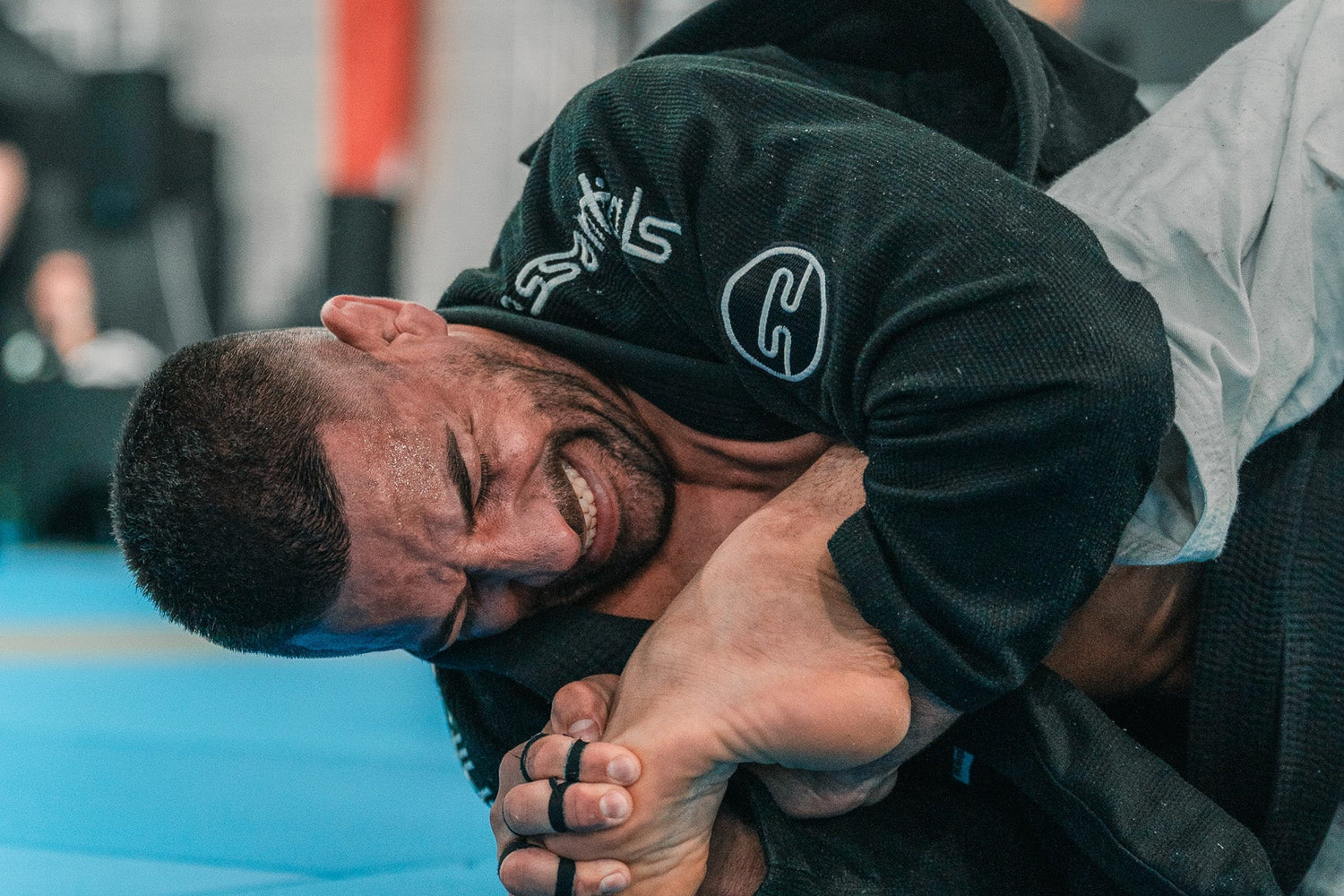 Two individuals in a grappling position on a blue mat in a jiu jitsu tournament