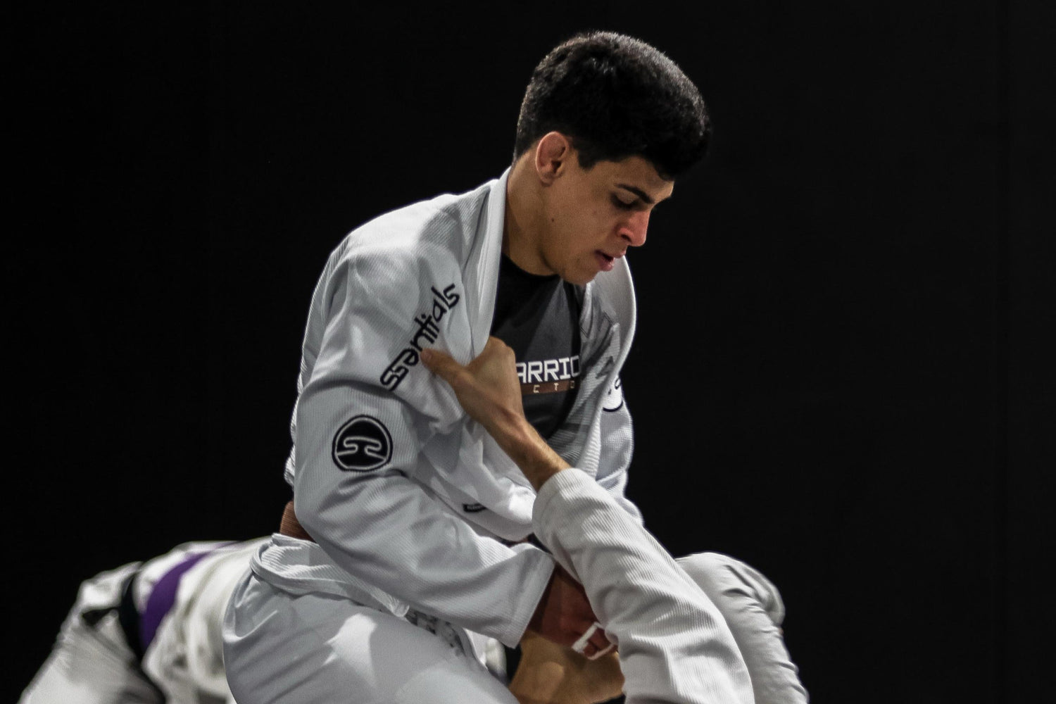 Two individuals practicing Jiu-Jitsu on a black mat.