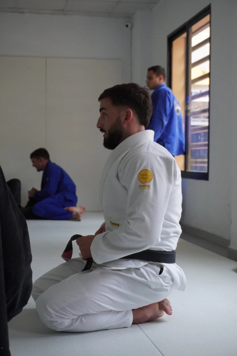 Jiu Jitsu athlete in white kimono with black belt kneeling in training room
