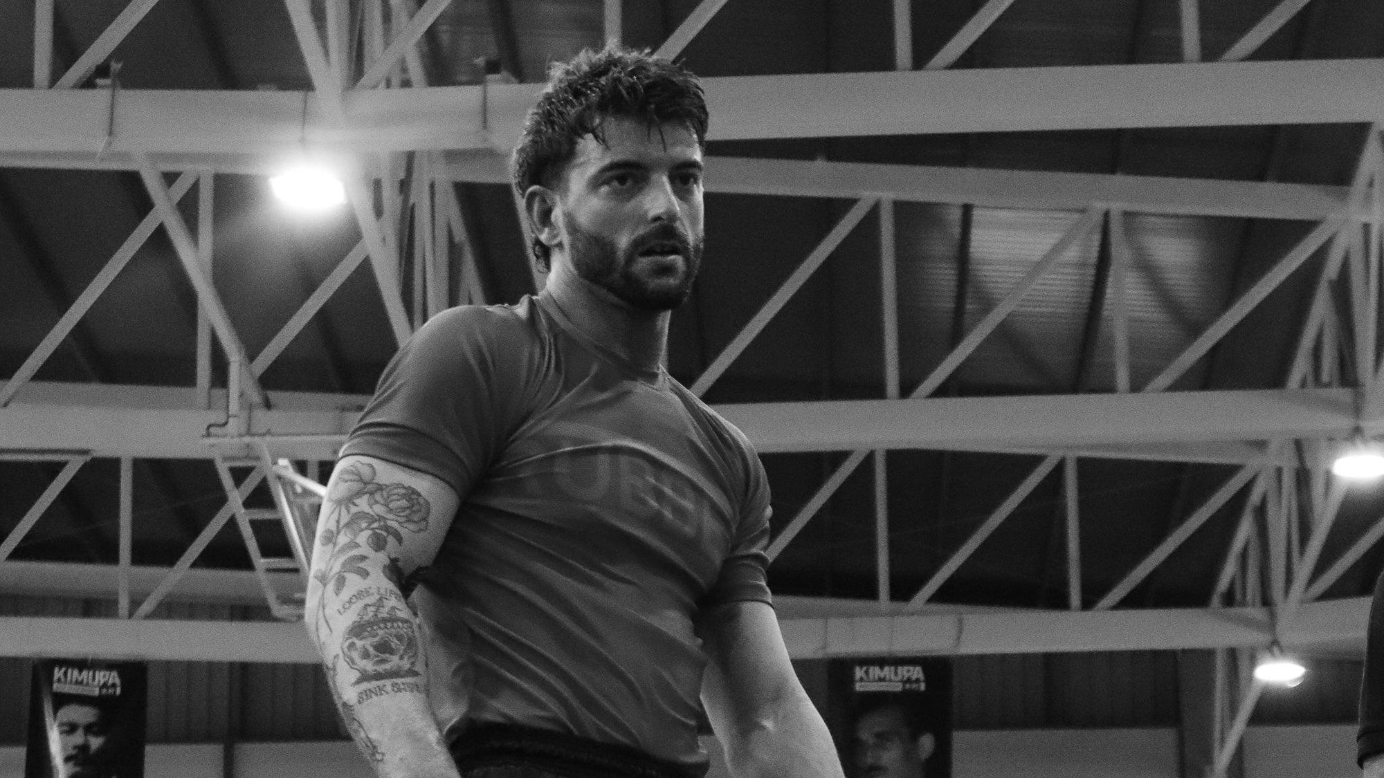 Man in athletic rashguard with tattooed arm training indoors, jiu jitsu gym background